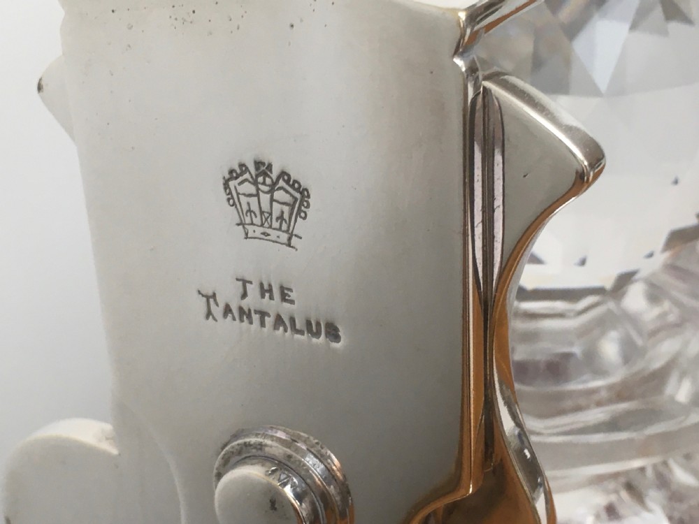 A silver-plated three-decanter tantalus featuring three cut-glass square decanters with facet-cut stoppers secured in a locking frame with a central handle. View V