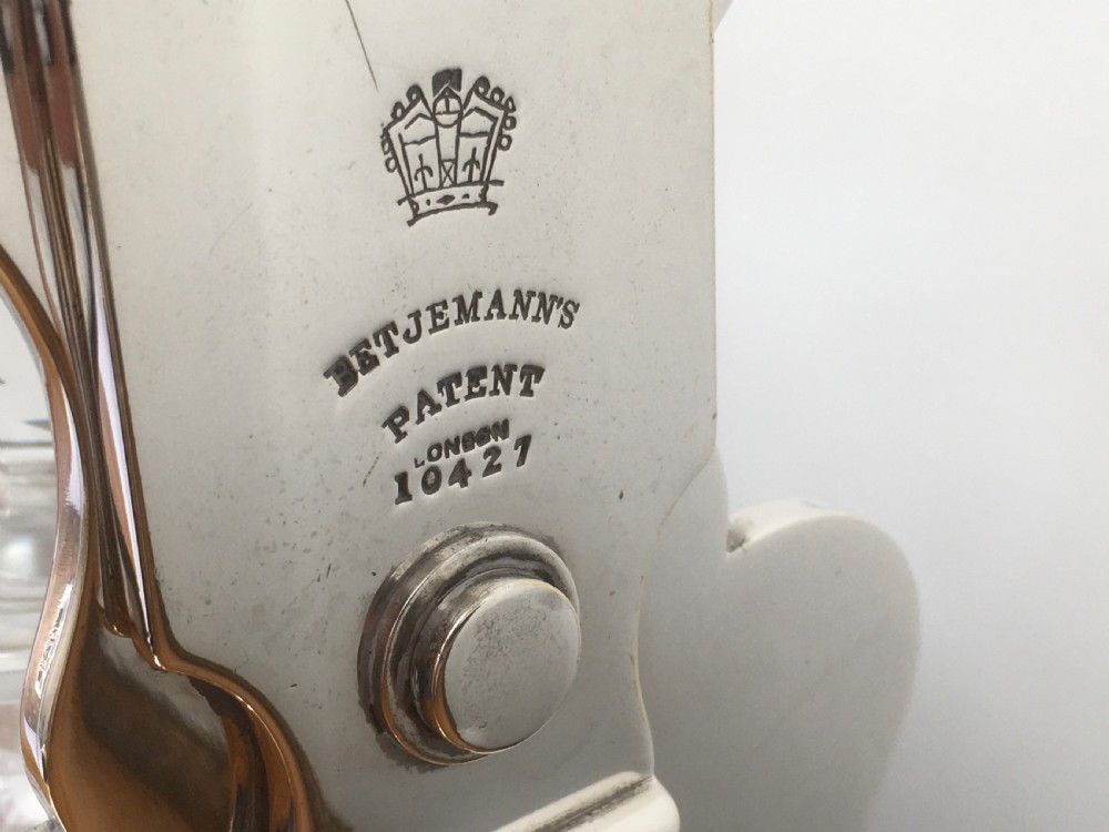 A silver-plated three-decanter tantalus featuring three cut-glass square decanters with facet-cut stoppers secured in a locking frame with a central handle. View VII
