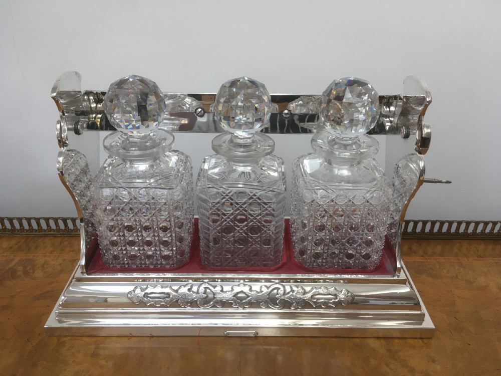 A silver-plated three-decanter tantalus featuring three cut-glass square decanters with facet-cut stoppers secured in a locking frame with a central handle. View VIII
