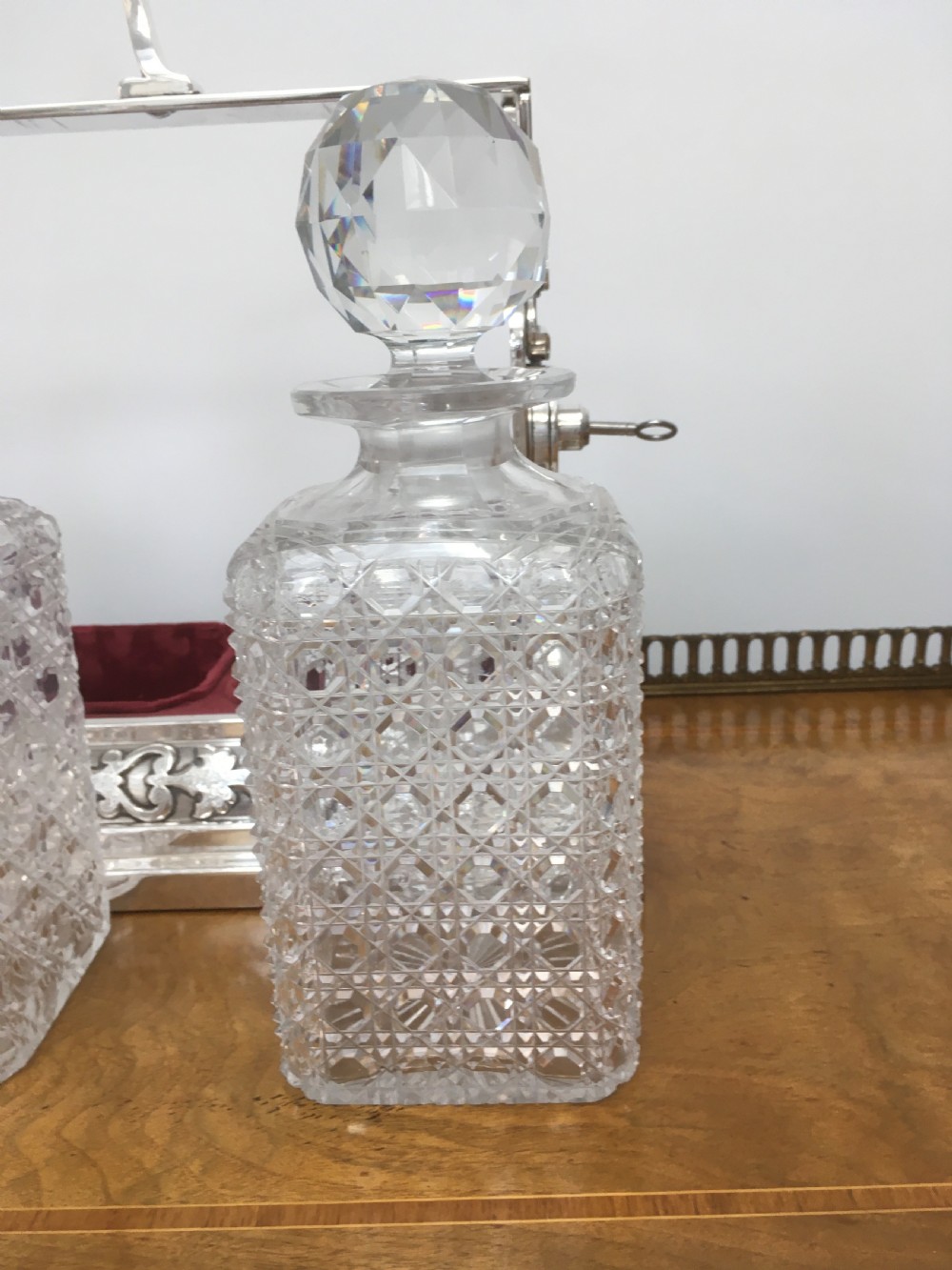 A silver-plated three-decanter tantalus featuring three cut-glass square decanters with facet-cut stoppers secured in a locking frame with a central handle. View XI