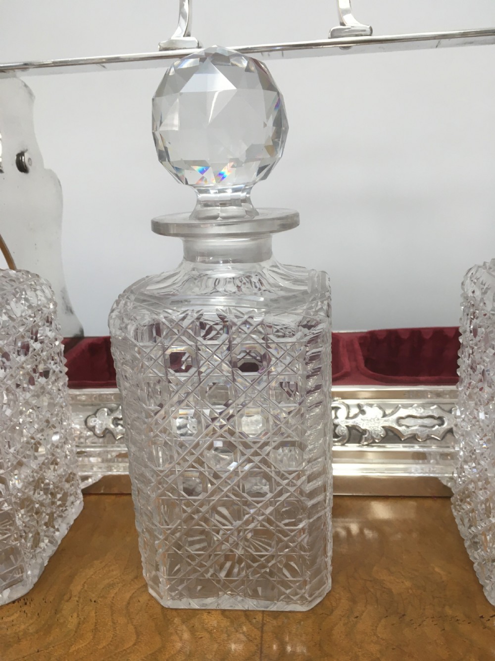 A silver-plated three-decanter tantalus featuring three cut-glass square decanters with facet-cut stoppers secured in a locking frame with a central handle. View XII