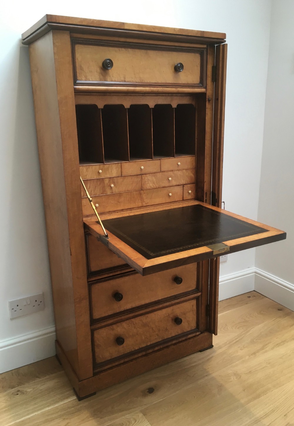 A tall Victorian birdseye maple secretaire Wellington chest featuring a hinged side locking bar, rosewood crossbanding, and a drop-down writing drawer revealing internal compartments.