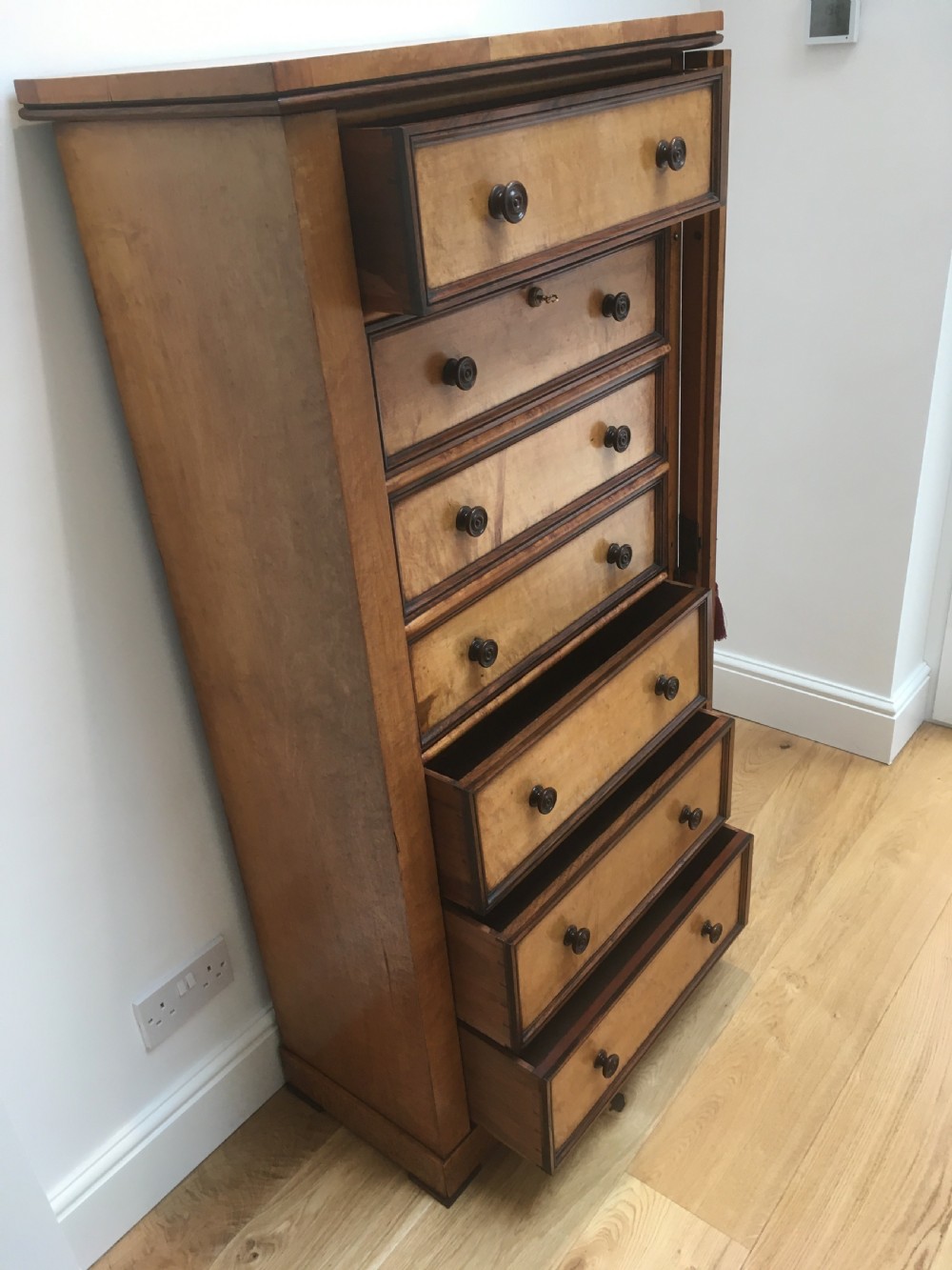 A tall Victorian birdseye maple secretaire Wellington chest featuring a hinged side locking bar, rosewood crossbanding, and a drop-down writing drawer revealing internal compartments. View IX