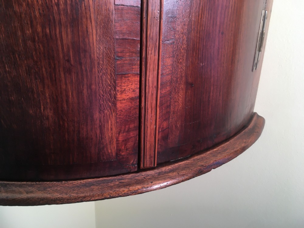A wall-mounted Georgian corner cabinet featuring a curved mahogany bow front, brass H-hinges, and a central keyhole with a decorative tassel. View IV