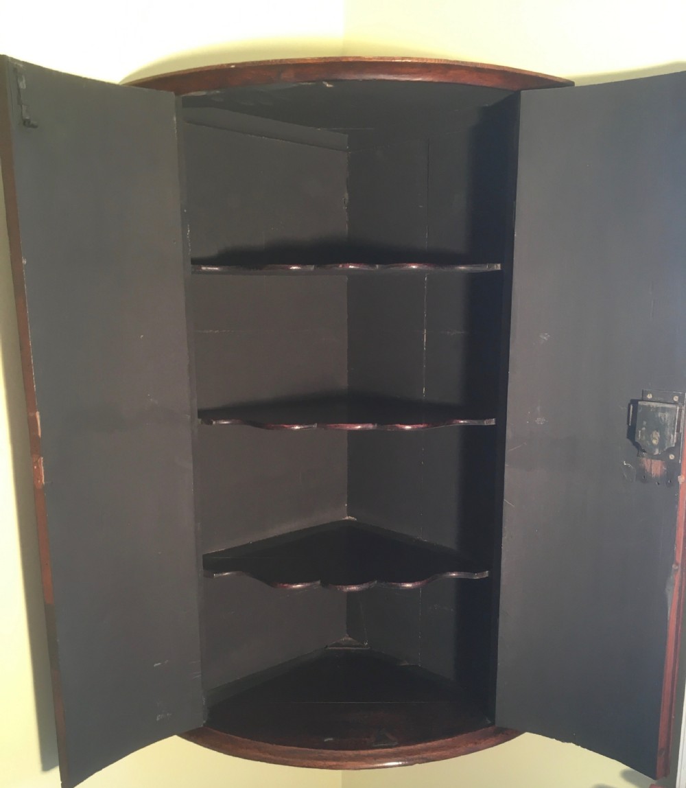 A wall-mounted Georgian corner cabinet featuring a curved mahogany bow front, brass H-hinges, and a central keyhole with a decorative tassel. View V
