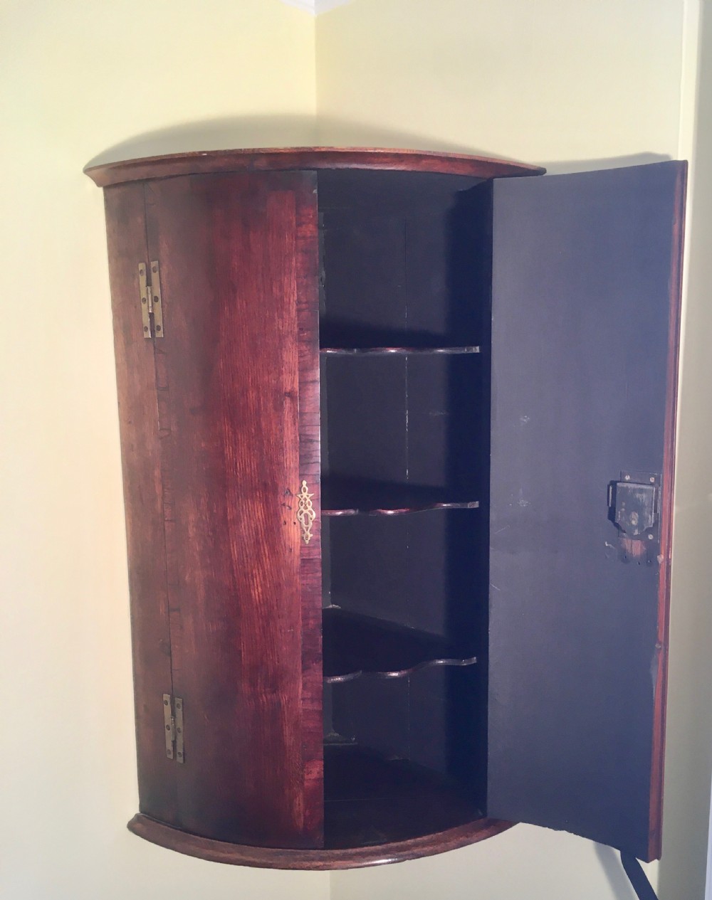 A wall-mounted Georgian corner cabinet featuring a curved mahogany bow front, brass H-hinges, and a central keyhole with a decorative tassel. View VII