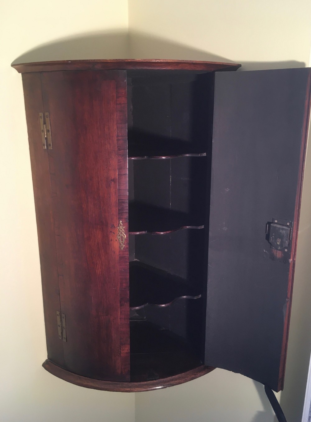 A wall-mounted Georgian corner cabinet featuring a curved mahogany bow front, brass H-hinges, and a central keyhole with a decorative tassel. View VIII