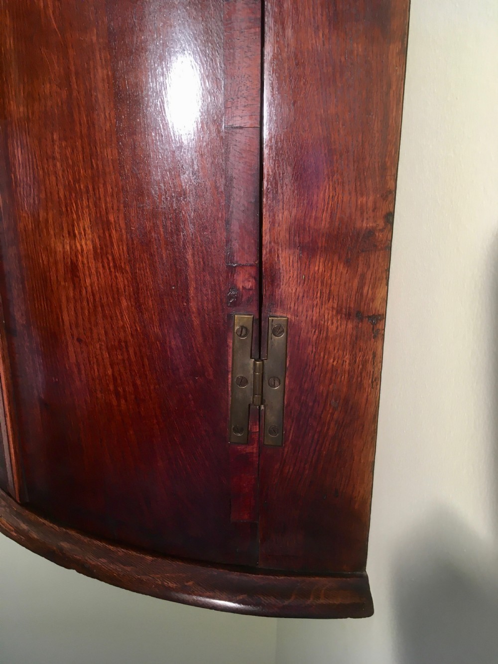 A wall-mounted Georgian corner cabinet featuring a curved mahogany bow front, brass H-hinges, and a central keyhole with a decorative tassel. View X