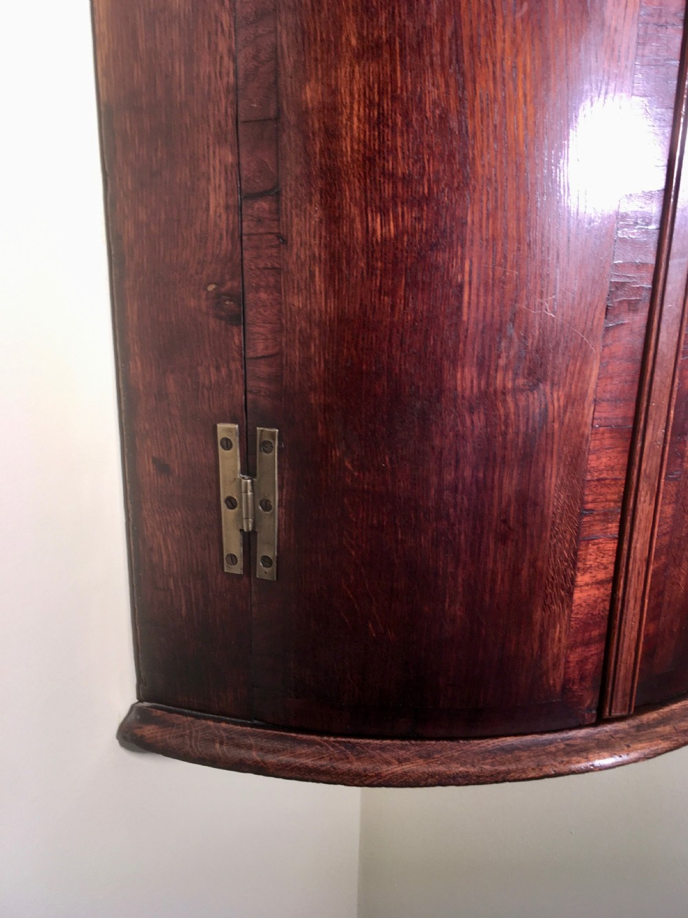 A wall-mounted Georgian corner cabinet featuring a curved mahogany bow front, brass H-hinges, and a central keyhole with a decorative tassel. View XI