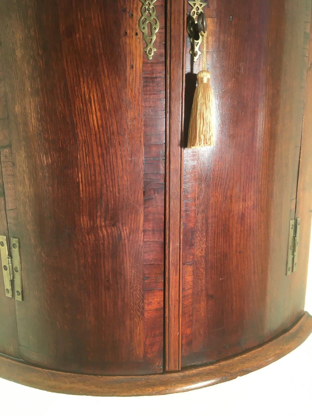 A wall-mounted Georgian corner cabinet featuring a curved mahogany bow front, brass H-hinges, and a central keyhole with a decorative tassel. View XII