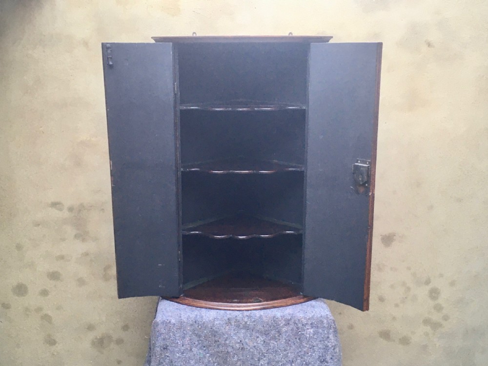 A wall-mounted Georgian corner cabinet featuring a curved mahogany bow front, brass H-hinges, and a central keyhole with a decorative tassel. View XVI