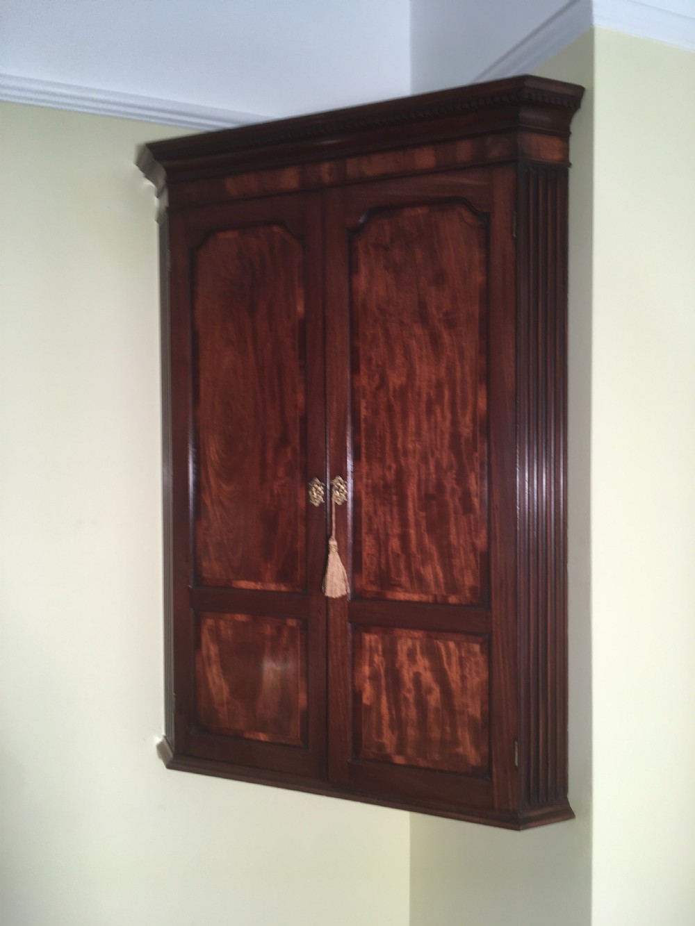 A wall-mounted Georgian mahogany corner cabinet featuring twin panelled doors, fluted side pilasters, and brass keyhole escutcheons. View II
