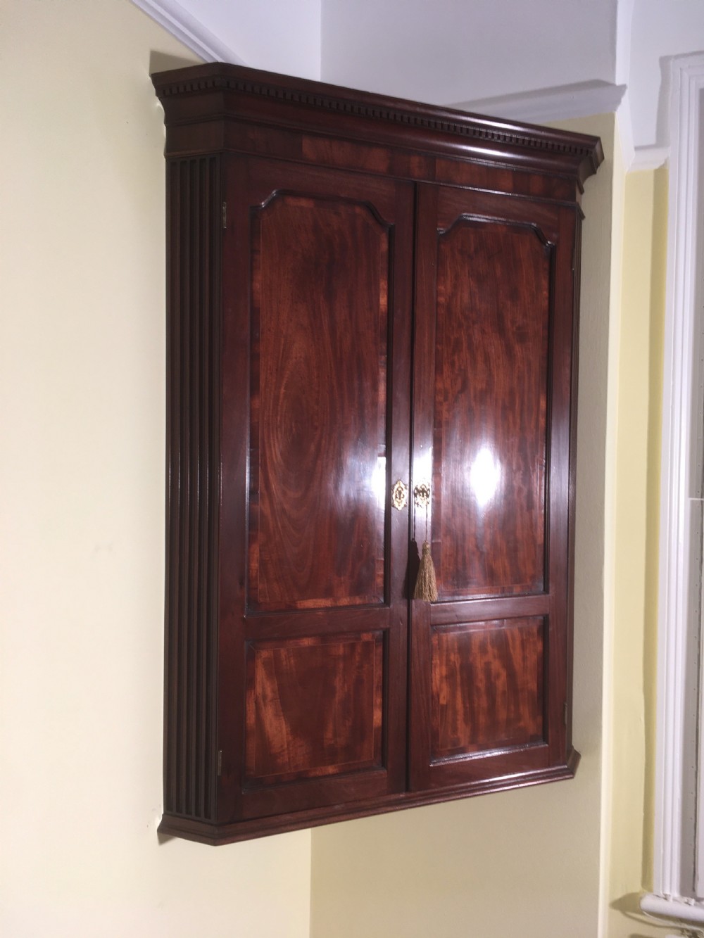 A wall-mounted Georgian mahogany corner cabinet featuring twin panelled doors, fluted side pilasters, and brass keyhole escutcheons. View III