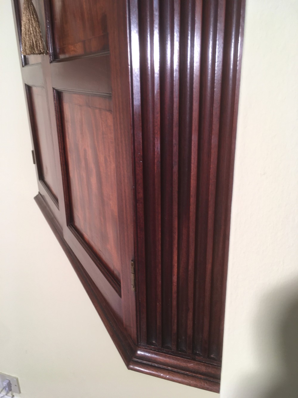 A wall-mounted Georgian mahogany corner cabinet featuring twin panelled doors, fluted side pilasters, and brass keyhole escutcheons. View V