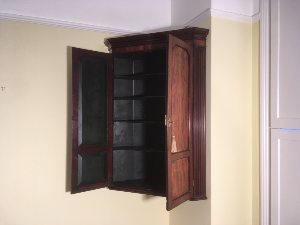 A wall-mounted Georgian mahogany corner cabinet featuring twin panelled doors, fluted side pilasters, and brass keyhole escutcheons. View VII