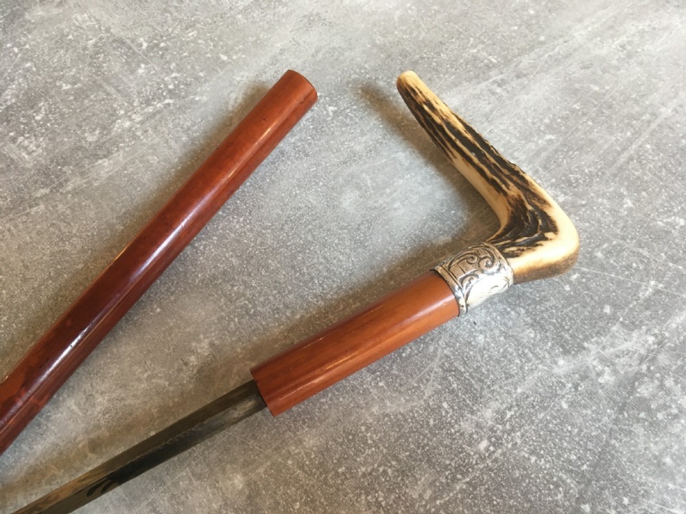 An antique Malacca wood walking stick featuring a carved stag antler handle and silver collar, drawn to reveal a long steel concealed blade. View V