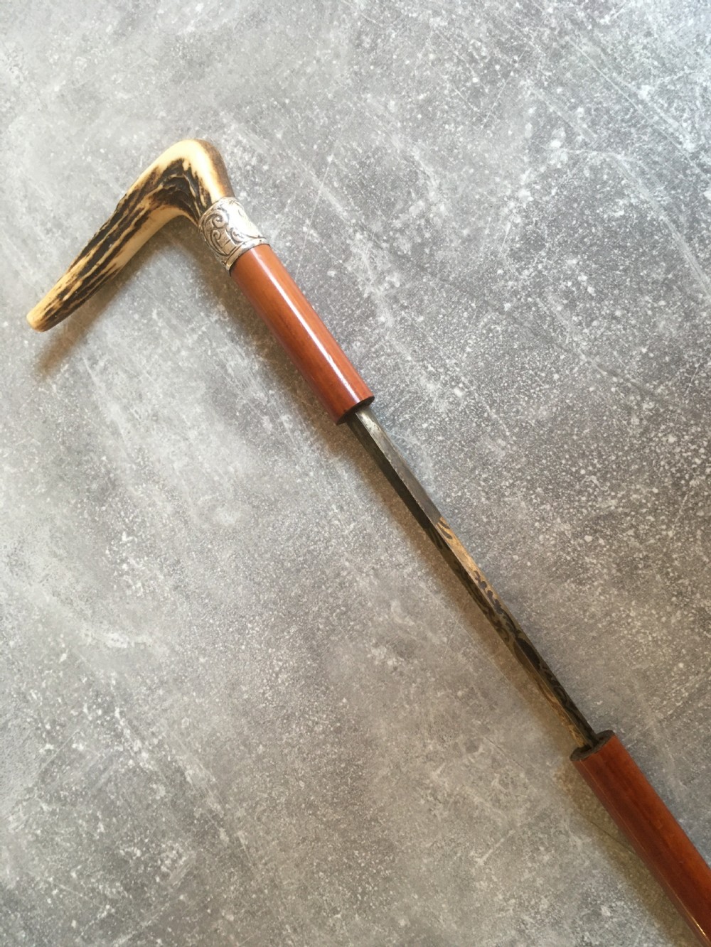 An antique Malacca wood walking stick featuring a carved stag antler handle and silver collar, drawn to reveal a long steel concealed blade. View XI