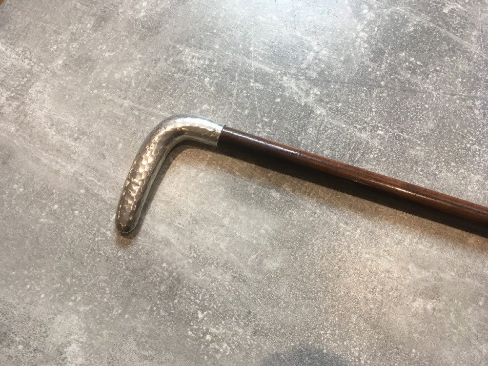 An antique walking stick featuring a hand-hammered silver L-shaped handle fitted to a tapered dark brown wooden shaft. View II