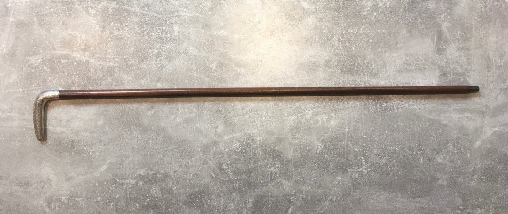 An antique walking stick featuring a hand-hammered silver L-shaped handle fitted to a tapered dark brown wooden shaft. View III