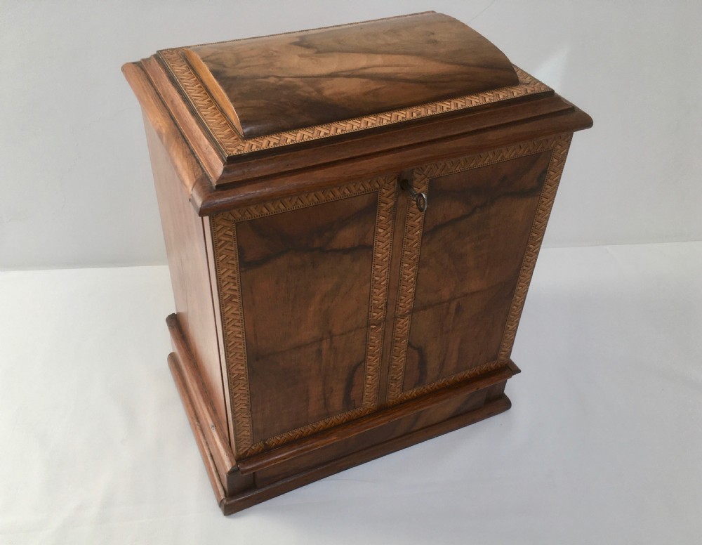 An inlaid walnut correspondence chest featuring geometric band inlay around figured wood panels, a domed lid, two front doors, and a central keyhole with a key inserted.