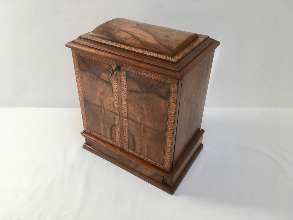 An inlaid walnut correspondence chest featuring geometric band inlay around figured wood panels, a domed lid, two front doors, and a central keyhole with a key inserted. View II