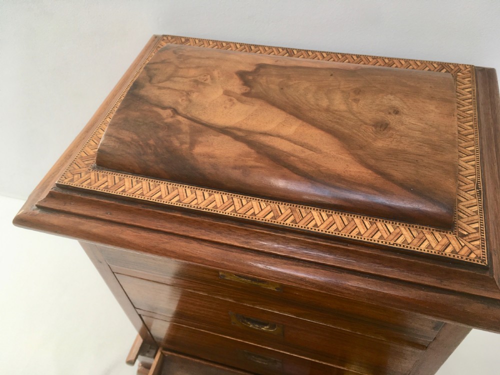 An inlaid walnut correspondence chest featuring geometric band inlay around figured wood panels, a domed lid, two front doors, and a central keyhole with a key inserted. View V