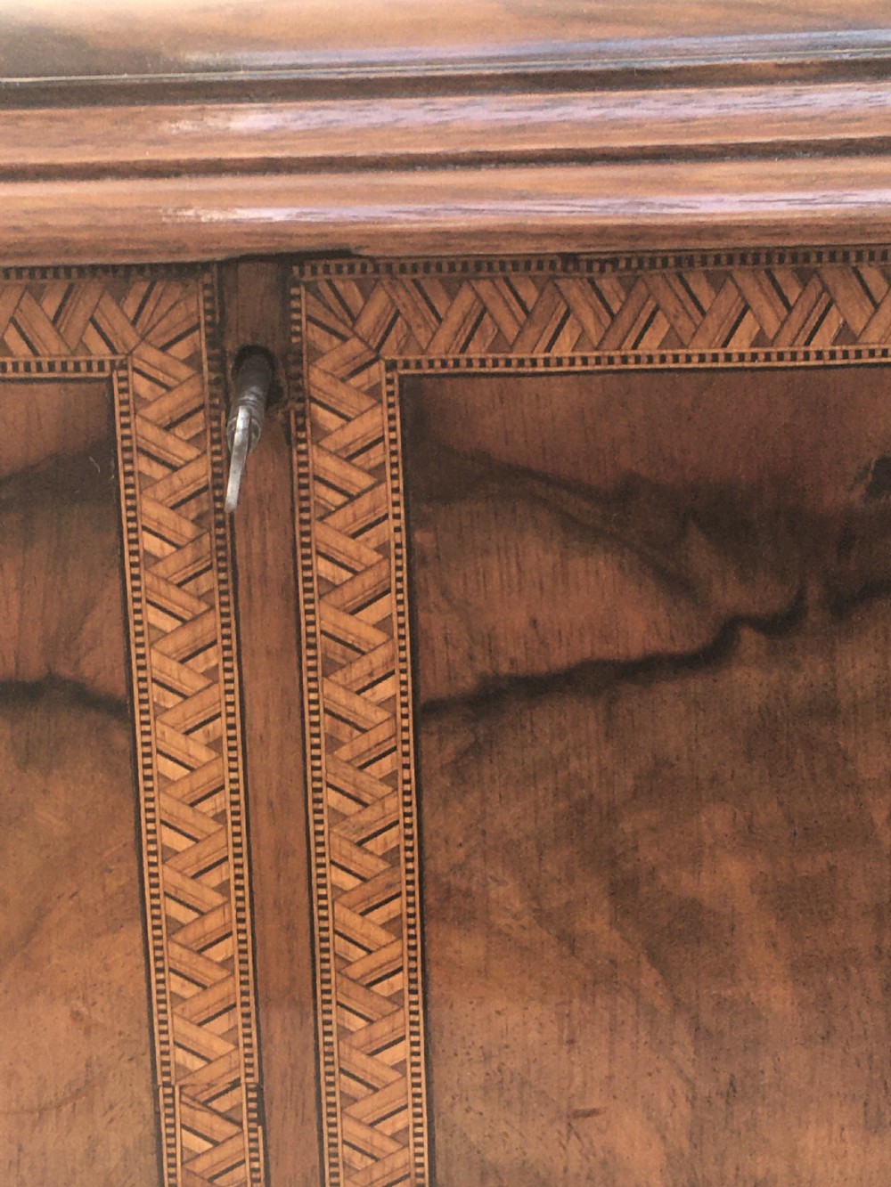 An inlaid walnut correspondence chest featuring geometric band inlay around figured wood panels, a domed lid, two front doors, and a central keyhole with a key inserted. View VII