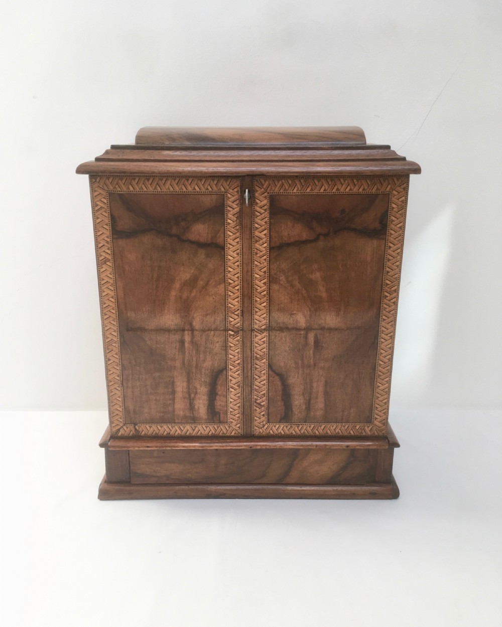 An inlaid walnut correspondence chest featuring geometric band inlay around figured wood panels, a domed lid, two front doors, and a central keyhole with a key inserted. View XI