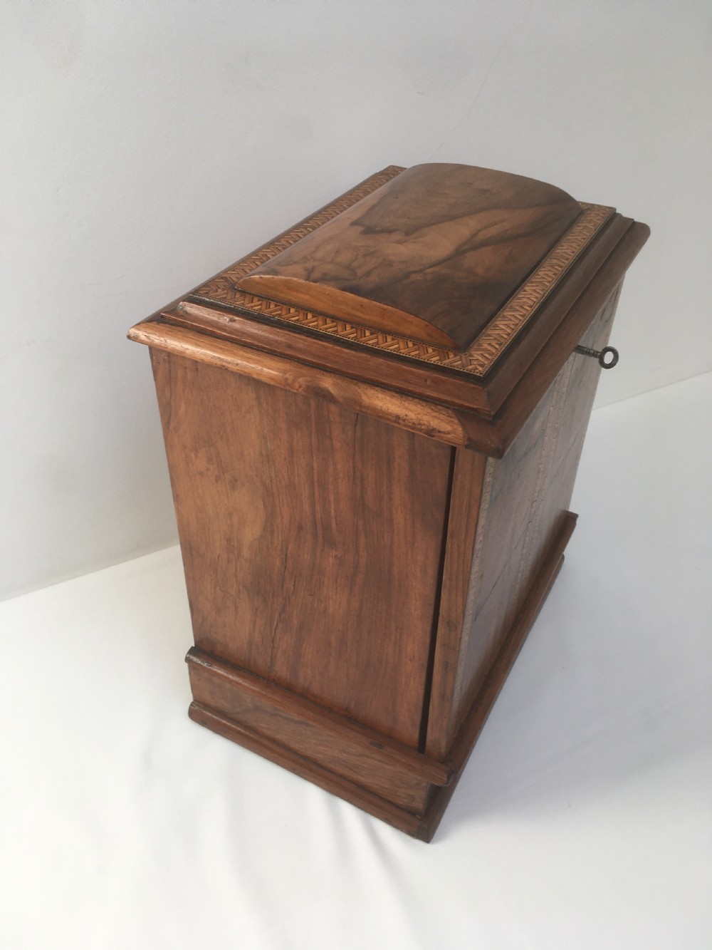 An inlaid walnut correspondence chest featuring geometric band inlay around figured wood panels, a domed lid, two front doors, and a central keyhole with a key inserted. View XII
