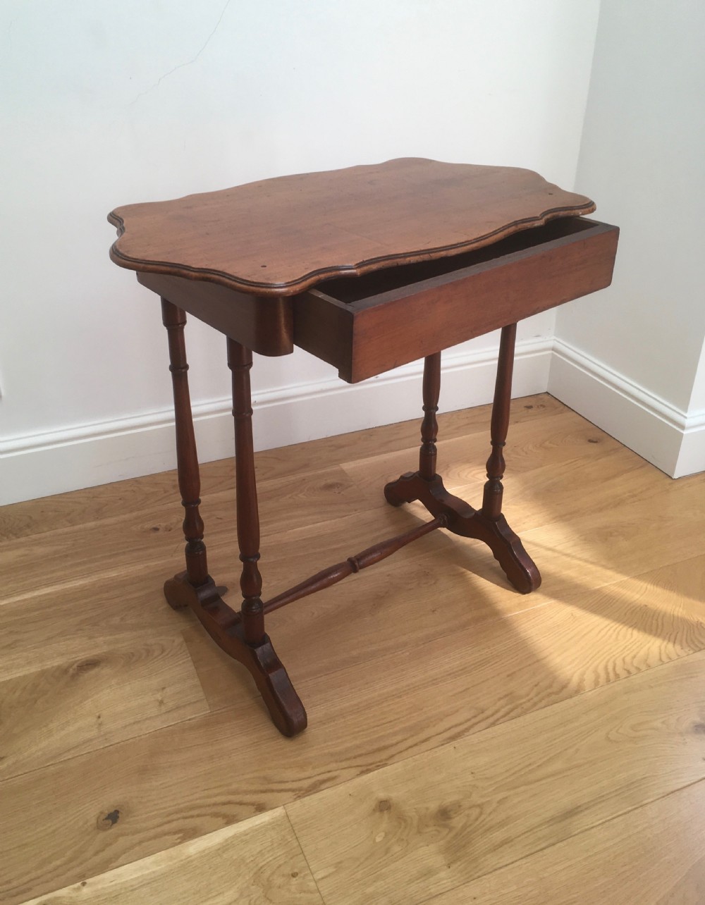 A Victorian mahogany side table featuring a serpentine top, turned legs with a stretcher base, and a single pull-out frieze drawer.
