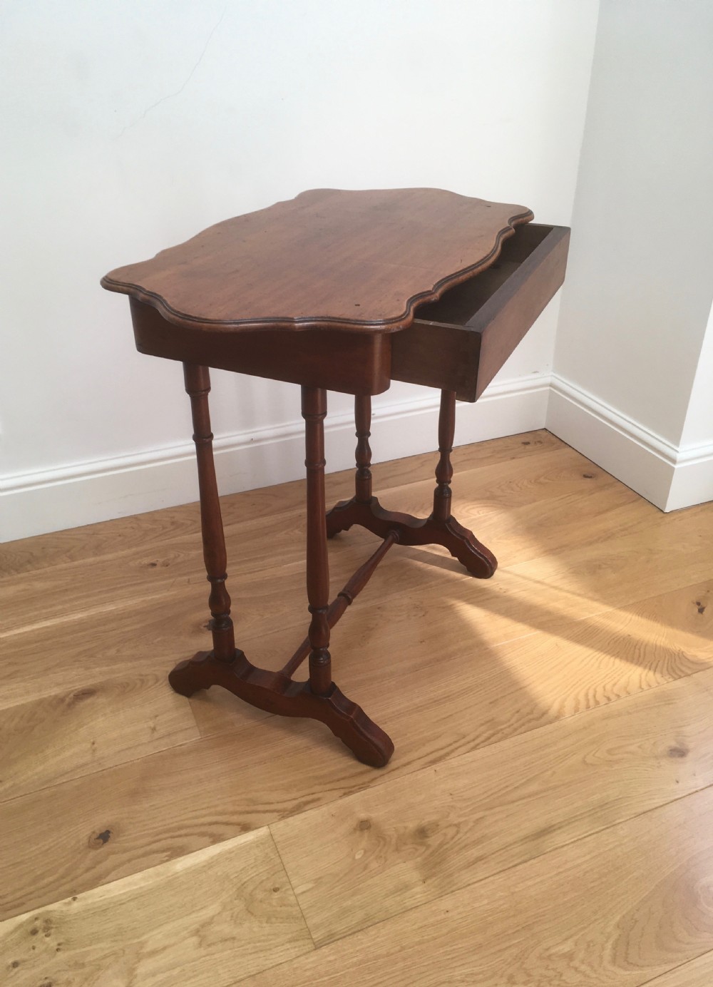 A Victorian mahogany side table featuring a serpentine top, turned legs with a stretcher base, and a single pull-out frieze drawer. View IV