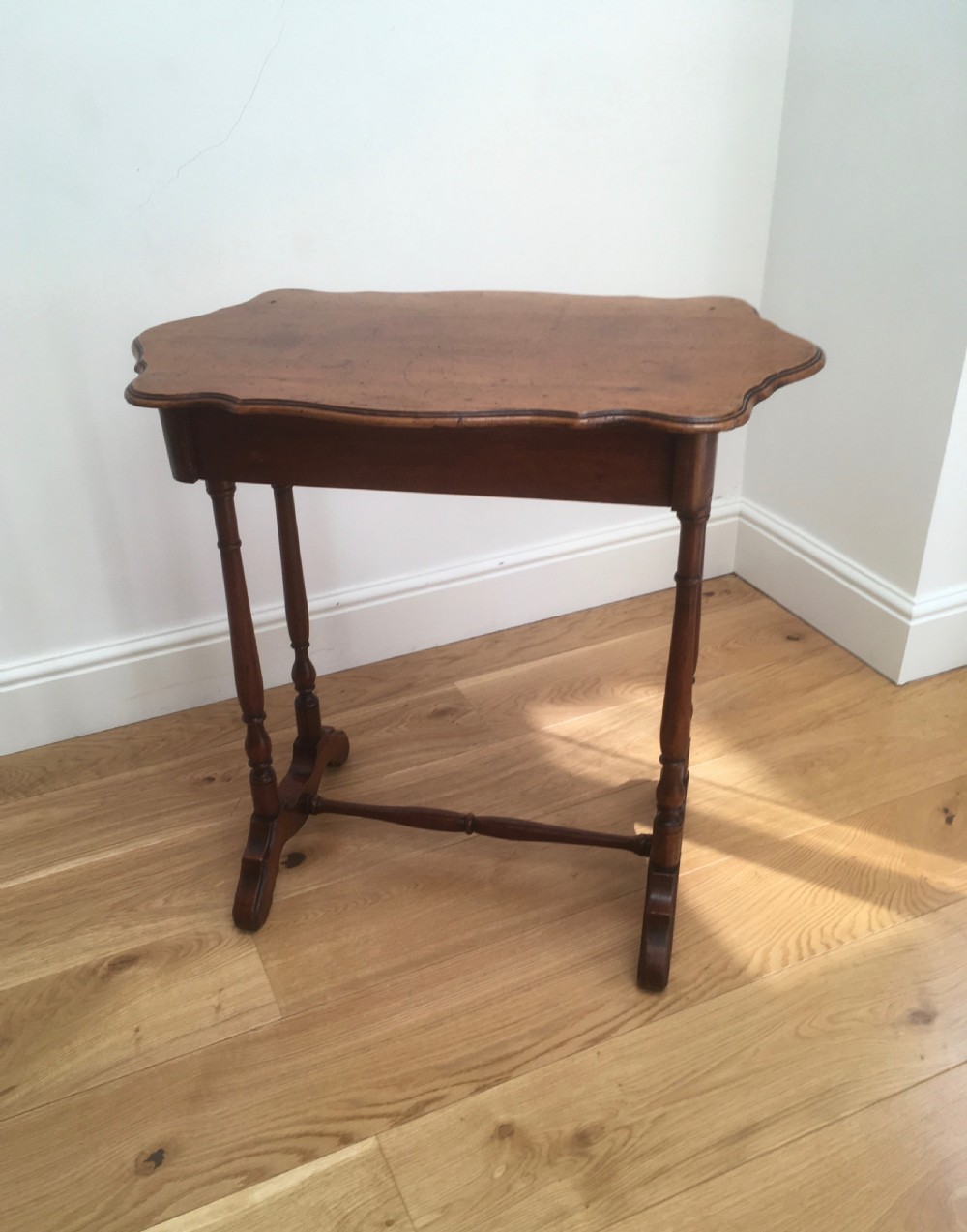 A Victorian mahogany side table featuring a serpentine top, turned legs with a stretcher base, and a single pull-out frieze drawer. View VI