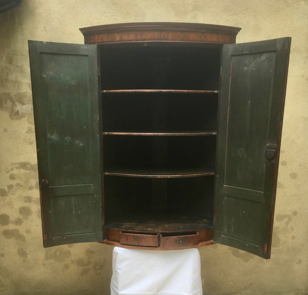 A Georgian mahogany bow-fronted corner cabinet featuring twin panelled doors, decorative inlay along the top cornice, and brass keyhole escutcheons. View II