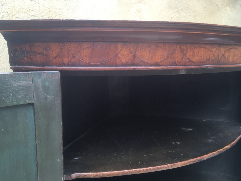 A Georgian mahogany bow-fronted corner cabinet featuring twin panelled doors, decorative inlay along the top cornice, and brass keyhole escutcheons. View IV