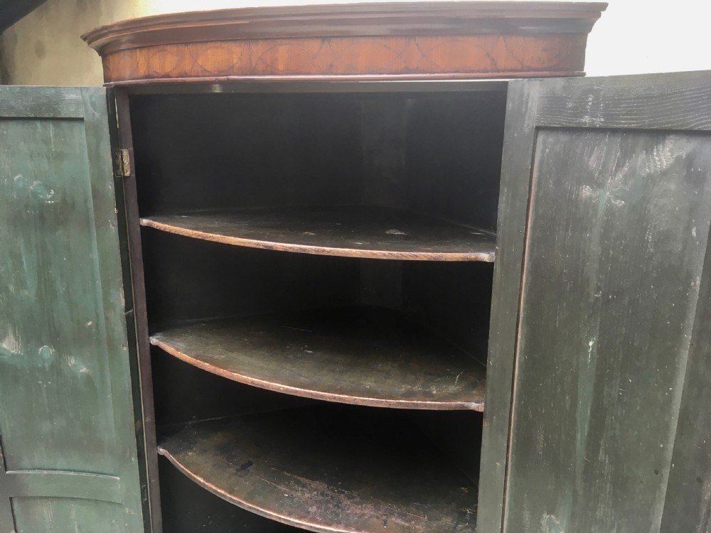 A Georgian mahogany bow-fronted corner cabinet featuring twin panelled doors, decorative inlay along the top cornice, and brass keyhole escutcheons. View V
