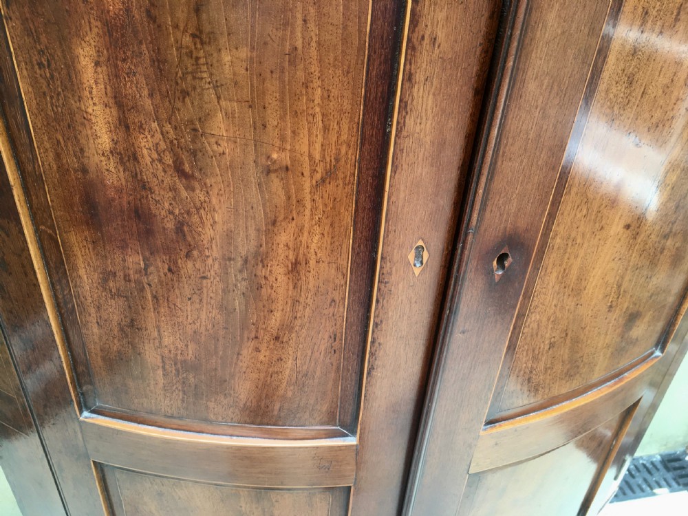 A Georgian mahogany bow-fronted corner cabinet featuring twin panelled doors, decorative inlay along the top cornice, and brass keyhole escutcheons. View VII