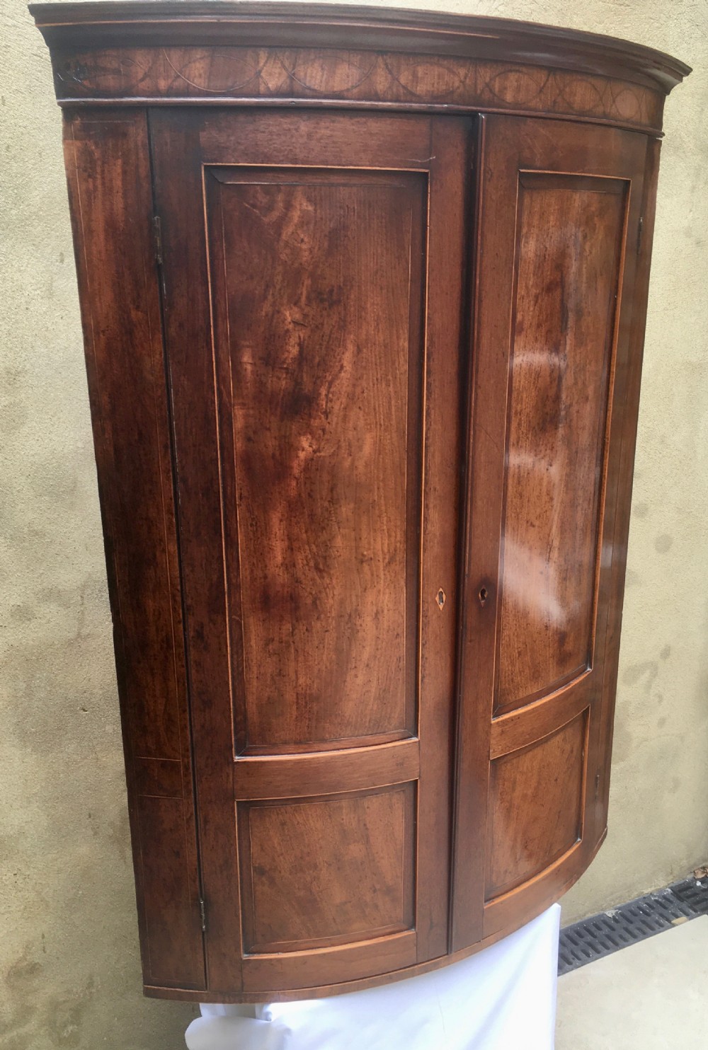 A Georgian mahogany bow-fronted corner cabinet featuring twin panelled doors, decorative inlay along the top cornice, and brass keyhole escutcheons. View VIII