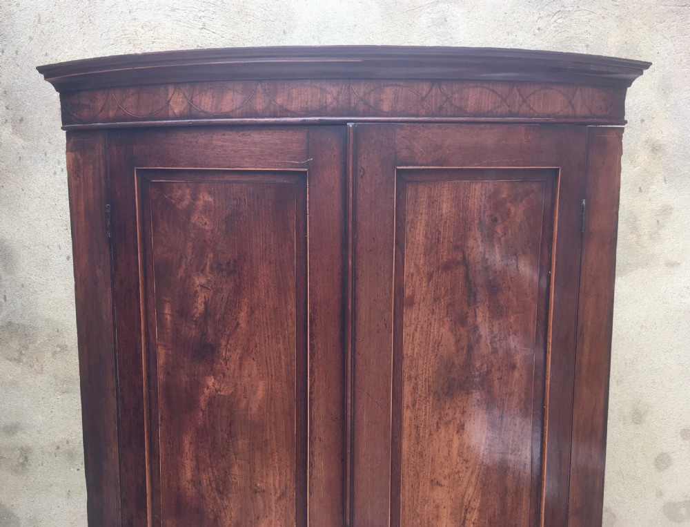 A Georgian mahogany bow-fronted corner cabinet featuring twin panelled doors, decorative inlay along the top cornice, and brass keyhole escutcheons. View XI