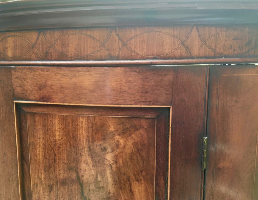 A Georgian mahogany bow-fronted corner cabinet featuring twin panelled doors, decorative inlay along the top cornice, and brass keyhole escutcheons. View XIII