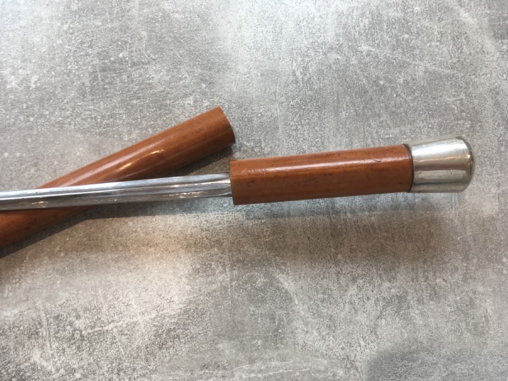 An antique Malacca cane walking stick featuring a smooth turned wood shaft, a brass ferrule at the tip, and a silver cap handle. View V