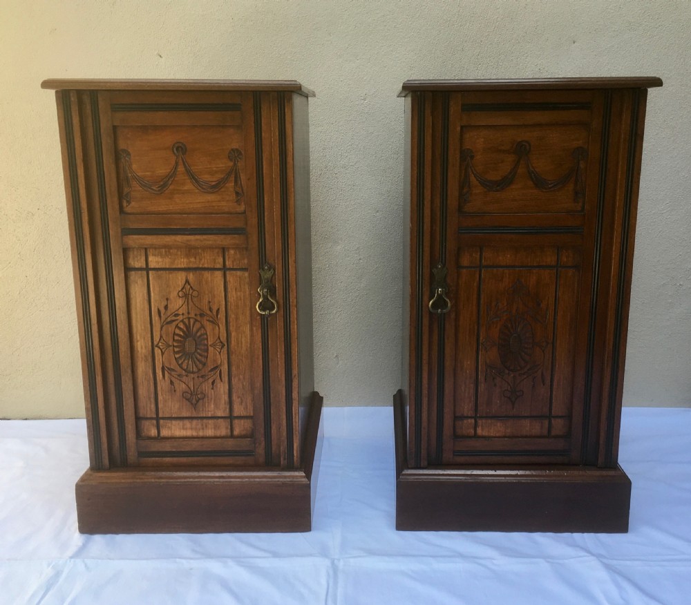 A matching pair of slim Edwardian mahogany bedside cabinets featuring carved swag decoration, single cupboards, brass handles, and solid plinth bases. View II