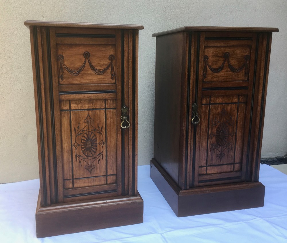 A matching pair of slim Edwardian mahogany bedside cabinets featuring carved swag decoration, single cupboards, brass handles, and solid plinth bases. View III
