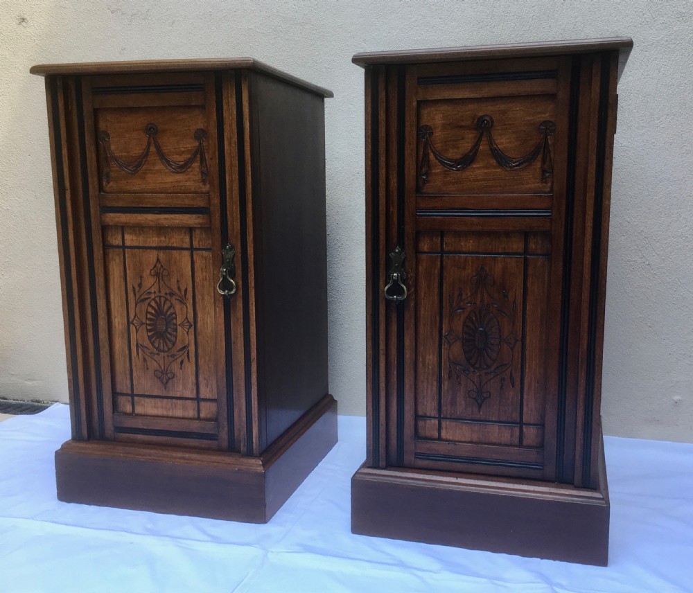 A matching pair of slim Edwardian mahogany bedside cabinets featuring carved swag decoration, single cupboards, brass handles, and solid plinth bases. View IV