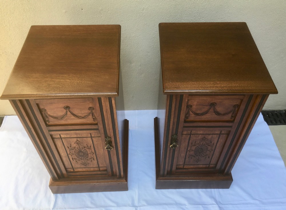 A matching pair of slim Edwardian mahogany bedside cabinets featuring carved swag decoration, single cupboards, brass handles, and solid plinth bases. View VIII