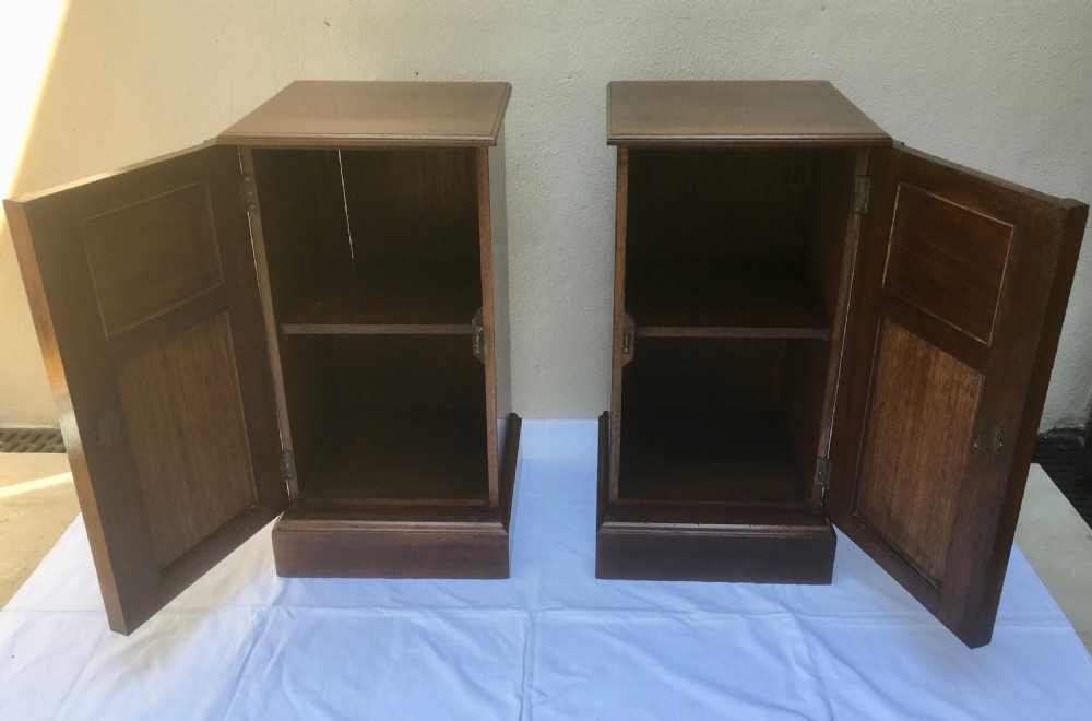 A matching pair of slim Edwardian mahogany bedside cabinets featuring carved swag decoration, single cupboards, brass handles, and solid plinth bases. View IX