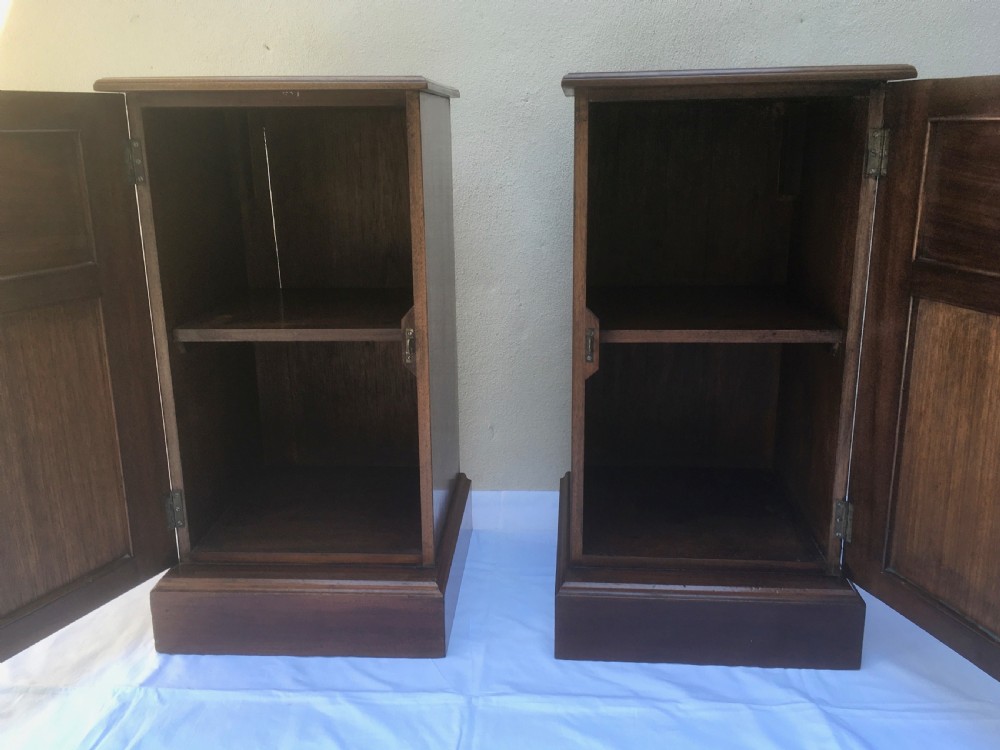 A matching pair of slim Edwardian mahogany bedside cabinets featuring carved swag decoration, single cupboards, brass handles, and solid plinth bases. View X