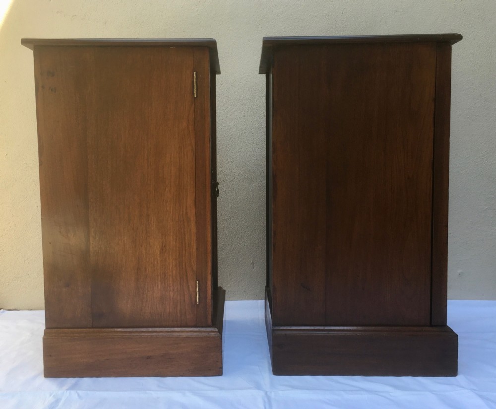 A matching pair of slim Edwardian mahogany bedside cabinets featuring carved swag decoration, single cupboards, brass handles, and solid plinth bases. View XII