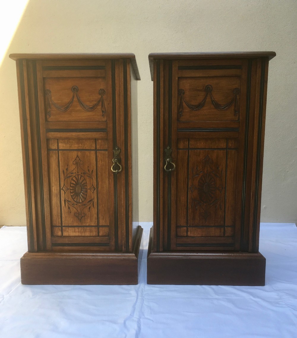 A matching pair of slim Edwardian mahogany bedside cabinets featuring carved swag decoration, single cupboards, brass handles, and solid plinth bases. View XVI