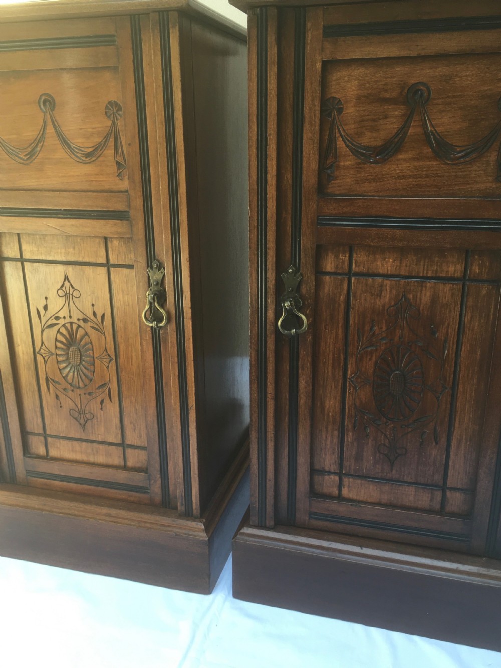 A matching pair of slim Edwardian mahogany bedside cabinets featuring carved swag decoration, single cupboards, brass handles, and solid plinth bases. View XVII