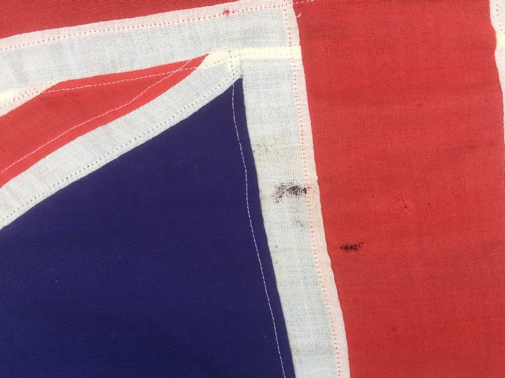 A rectangular Second World War Royal Navy White Ensign flag featuring a white field with a red Saint Georges Cross, a Union Jack canton, and a stitched canvas edge with rope lanyard. View V